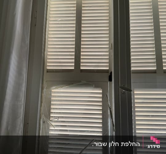 חלון עם זכוכית שבורה ותריסים סגורים